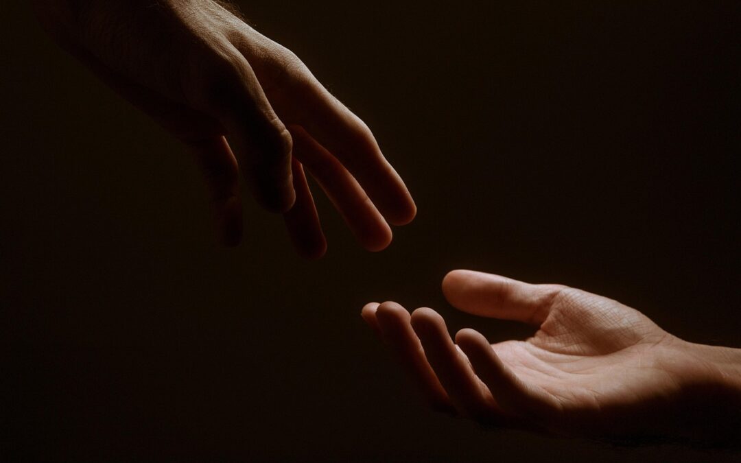 Photo of two hand reaching for each other.