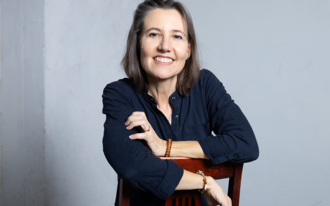 Photo of Rachel S. Heslin, catalyst and facilitator. She is looking straight into the camera, arms folded over the back of a chair. Her expression is calm, open, confident and strong. Photo credit Mark Maryanovich.